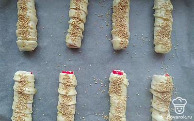 Оберните крабовые палочки по кругу полоской теста, выложите на противень. Взбейте яйцо и смажьте им выпечку. Посыпьте сверху кунжутом. Выпекайте в разогретой до 180 ℃ духовке 30 минут.