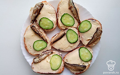 Нарезной батон обжарьте на сковороде. Одну сторону намажьте сливочным сыром. Огурец нарежьте наискосок тонким слайсом и уложите на один край бутерброда. Положите на бутерброды по одной шпроте. Рядом с огурцом положите по одной чайной ложки красной икры.