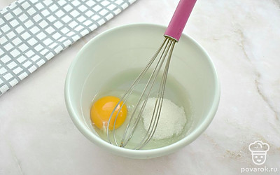 Разбейте в миску куриное яйцо. Всыпьте к яйцу столовую ложку сахара и щепотку соли. Взбейте ингредиенты венчиком.