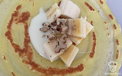 Выложите на блин ложку сгущенного молока, орехи и банан. Сверните в конверт.