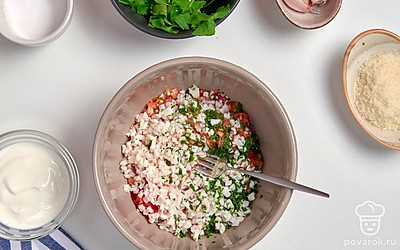 Приготовьте начинку. Из помидоров извлеките мякоть с помощью чайной ложки. Мелко нарежьте отварного кальмара, чеснок, петрушку. Смешайте нарезанные ингредиенты в миске с мякотью помидоров, заправьте сметаной, посолите, поперчите и перемешайте.