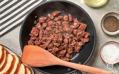 Пожарьте свиную печень. Для этого сковороду поставьте на огонь, влейте растительное масло, подогрейте и выложите лук. Пожарьте до румяности в течение 3-5 минут, добавьте кусочки печени. Посолите, поперчите и жарьте, помешивая, 5-7 минут. Снимите с огня и остудите.