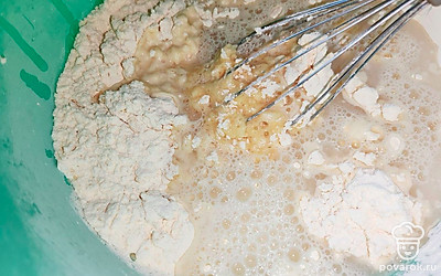 Добавьте прсеянную муку. Постепенно добавляйте воду комнатной температуры (или чуть теплее). Сначала добавьте один стакан. 