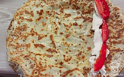 Выложите на блинчик творожный сыр и тонко нарезанный помидор. Сверните начинку в трубочку. 