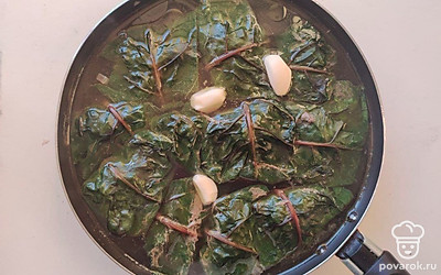 Накрутите голубцы. Небольшую порцию начинки выложите на широкую часть свекольного листа и заверните его таким образом, чтобы не было открытых краев. Голубцы сложите в сотейник и залейте кипятком. Вода должна покрывать голубцы на 1 см. Поставьте сотейник с голубцами на огонь, доведите до кипения, затем уменьшите огонь до минимума и варите 30 — 35 минут. Снимите сотейник с огня и положите в него целые зубчики чеснока, оставьте голубцы под крышкой на 5 — 7 минут.