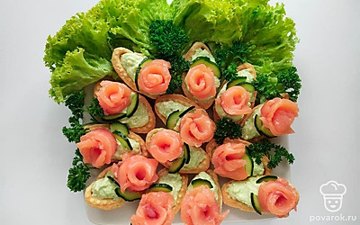 Скрутите кусочки рыбного филе в форме розочки и выложите на тарталетку, украсьте съедобные цветы листиками из огурца. Выложите на большую плоскую тарелку листья салата и петрушки, а на них готовые тарталетки.