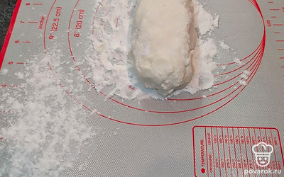 Достаньте творожную массу из холодильника, силиконовый коврик либо доску присыпьте мукой, выложите на муку тесто и сформируйте колбаску.