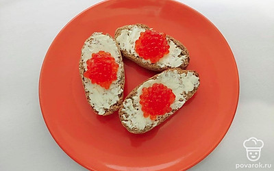 Достаньте их холодильника масло и дайте ему согреться при комнатной температуре. Намажьте его на хлебцы тонким аккуратным слоем и выложите на каждый по чайной ложке красной икры.