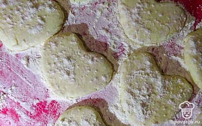 Начните формировать сырники-сердечки. Возьмите одну столовую ложку смеси, скатайте шарик, а затем из него сделайте сердечко. Положите на доску и с помощью лопатки придайте ему плоскую ровную форму. Доску обязательно посыпьте мукой, иначе сырники прилипнут к доске. 