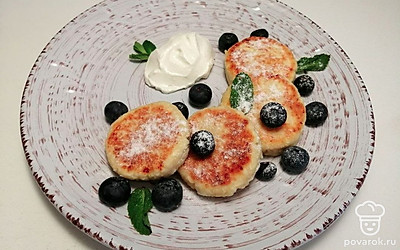 Готовые сырники подавайте горячие к столу, дополните их свежей сметаной и спелыми ягодами, для придачи сочности и сладости блюду.