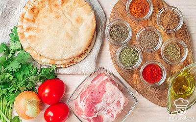 Для того, чтобы правильно приготовить греческий гирос, необходимо растолочь специи. Лучше делать это вручную, поэтому заранее подготовьте деревянную ступку и пестик. Вымойте и обсушите бумажными полотенцами мясо. Помидоры помойте, лук очистите от шелухи. Ополосните зеленый лук и веточки кинзы.