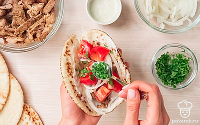 Сформируйте гирос. Лепешки немного согрейте на сухой сковороде, обжарив с одной стороны в течение 3-4 минут. Каждую питу немного надрежьте вдоль и смажьте внутри небольшим количеством соуса дзадзики. Затем выложите в лепешку свинину, лук, помидоры и посыпьте сверху кинзой.