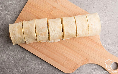 Лаваш аккуратно скатайте в рулет и разделите острым ножом на 7-8 равных частей.