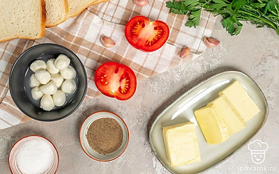 Моцареллу нарежьте тонкими ломтиками. Помидор помойте и нарежьте кружками. Чеснок очистите, мелко порубите или пропустите через пресс. Разогрейте духовку до 200 градусов и застелите противень пергаментом.