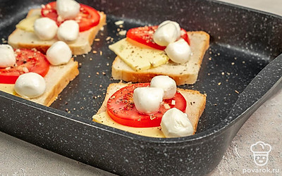 Подготовьте тосты к запеканию. На противень, застеленный пергаментом, выложите ломтики хлеба и положите на каждый по тонкому кусочку сливочного масла. Разложите на тосты нарезанный помидор. Присыпьте солью и перцем по вкусу и мелко нарезанным чесноком. После накройте тосты ломтиками моцареллы.