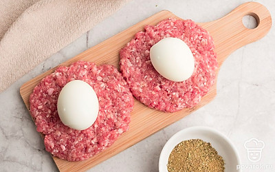 Фарш разделите на несколько частей, скатайте в шарики и разомните в лепешки толщиной 8-10 мм. В центр каждой из них выложите вареное яйцо. Аккуратно слепите котлету с яйцом внутри.