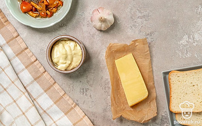 Натрите сыр на крупной терке. Почистите чеснок, пропустите через пресс. Петрушку вымойте, дайте воде стечь и мелко нарежьте. Откройте баночку с грибами, откиньте необходимое количество на дуршлаг, чтобы избавиться от лишнего маринада. Подготовьте противень, включите духовку на 180 градусов.