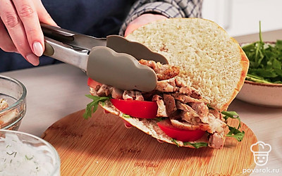 Соберите гирос. В разрезаную питу положите 2 ст. л. соуса. На него положите рукколу и помидоры. Сверху распределите кусочки курицы.. Так же оформите остальные порции гироса.