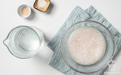 Приготовьте опару. В теплой воде размешайте сахар и тонкой струйкой всыпьте дрожжи. Перемешайте до полного растворения сахара. Оставьте массу на 15 минут в теплом месте без сквозняков, чтобы образовались пузырьки, а масса увеличилась в три раза.