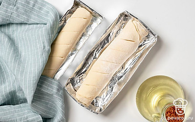 Подготовьте форму и багеты к выпечке. Воспользуйтесь специальной формой для багетов или сделайте ее из фольги. Для этого сложите ее в 3-4 слоя и сформируйте бортики — форма должна быть чуть больше, чем багет. Смажьте форму растительным маслом и слегка присыпьте мукой. Края согните, формируя "лодочку", и уложите в нее заготовки багетов. Накройте багеты полотенцем и поставьте в тепло на полчаса.