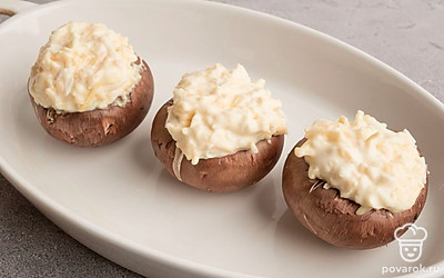 У шампиньонов шляпки отделите от ножек и поместите начинку в образовавшееся углубление. Поместите фаршированные шампиньоны в подходящую по размеру форму для выпечки. Запекайте в заранее разогретой до 180 градусов духовке в течение 20 минут.