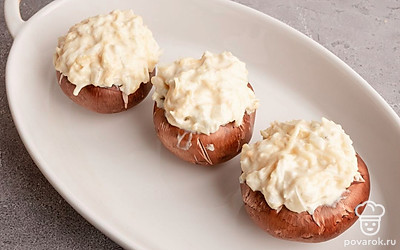 У шампиньонов шляпки отделите от ножек и поместите начинку в образовавшееся углубление. Поместите фаршированные шампиньоны в подходящую по размеру форму для выпечки. Запекайте в заранее разогретой до 180 градусов духовке в течение 20 минут.