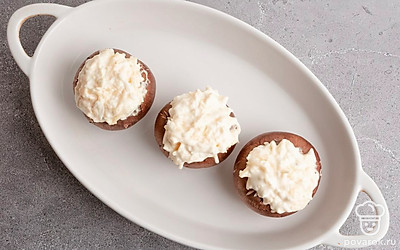 У шампиньонов шляпки отделите от ножек и поместите начинку в образовавшееся углубление. Поместите фаршированные шампиньоны в подходящую по размеру форму для выпечки. Запекайте в заранее разогретой до 180 градусов духовке в течение 20 минут.