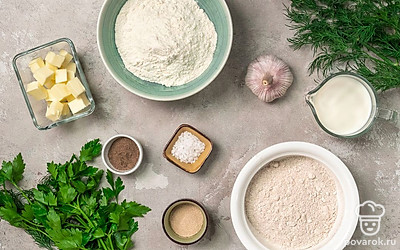 Муку пшеничную и ржаную просейте и соедините в миске. Молоко подогрейте до температуры 40 градусов. Чеснок очистите и пропустите через пресс. Сливочное масло размягчите. Петрушку и укроп переберите, промойте, просушите и мелко нарежьте. Помидоры и огурцы помойте, у помидоров удалите плодоножку. Затем огурцы и помидоры нарежьте дольками. Разогрейте духовку до 200 градусов и застелите противень пергаментом.