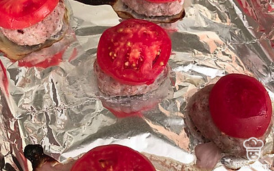 Когда мясо будет готово, кладем на каждый биточек помидор. Отправляем еще на 5 минут допекаться.