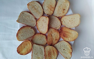 Батон нарежьте тонкими ломтиками и поджарьте на сухой сковороде по 2 минуты с каждой стороны до золотистости. Натрите поджаренные ломтики хлеба чесноком с обеих сторон.