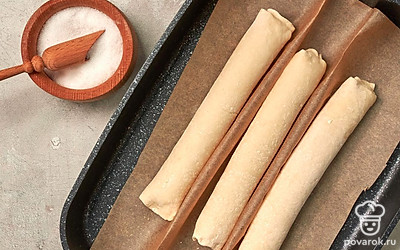 Присыпьте мукой рабочую поверхность. Каждую часть теста раскатайте в лепешку толщиной 0,5 см, сверните в рулет и защипните края. Противень застелите пергаментом.