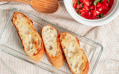 Подготовьте багет. Кусочки хлеба уберите в духовку, разогретую до 70-80 градусов. Слегка подсушите 7-10 минут. Сделайте начинку, пока готовится багет. Смешайте базилик, чеснок, помидоры, оливковое и чесночное масло. Посолите.