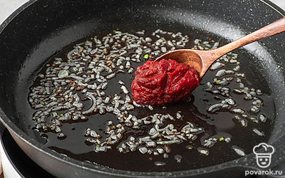 Выложите на сковороду к луку томатную пасту. Перемешайте и обжарьте смесь в течение 1 минуты.