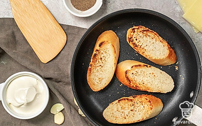 Приготовьте основу. На разогретую сковороду налейте растительное масло. Ломтики багета обжарьте с двух сторон. Пока хлеб не остыл, натрите его чесноком.