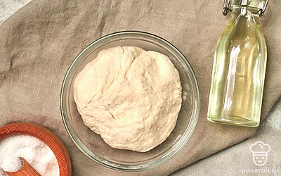 Замесите тесто. Смешайте муку с солью, добавьте к ней опару, перемешайте. Не переставая вымешивать тесто, постепенно добавьте холодную воду. Вымешивайте тесто 10 минут. Затем миску смажьте растительным маслом, выложите в нее тесто, накройте влажным полотенцем. Оставьте в теплом месте на 2 часа.