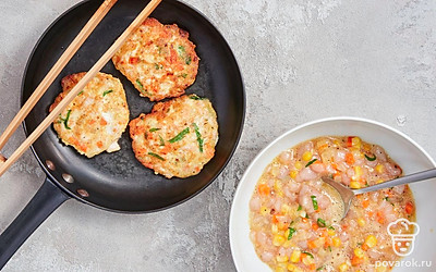 Приготовьте блюдо. В миске смешайте лук с морковью, петрушку, курицу, кукурузу, чеснок. Влейте сырые яйца, всыпьте соль и специи, хорошо все размешайте. Сформируйте из полученной смеси оладьи. Выложите их на сковороду и обжарьте по 3 минуты с каждой стороны.