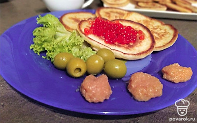 Выложите оладьи на блюдо, украсив листьями салата. В отдельных пиалах подайте икру и сливочное масло.