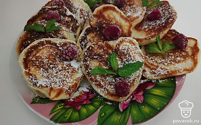 Выложите оладья на тарелку и посыпьте их сахарной пудрой, малиной и листочками мяты.