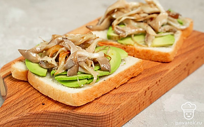 Приготовьте тосты. Авокадо нарежьте тонкими ломтиками, после чего выложите их на тосты. Сверху распределите жареные грибы и подайте блюдо к столу.