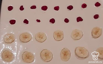 Вылейте тесто на противень, застеленный пергаментной бумагой или ковриком, сверху украсьте бананом и ягодами.