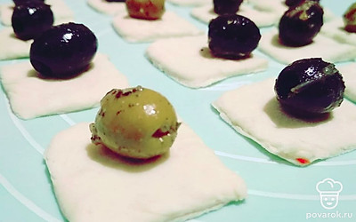 Разморозьте готовое слоено-дрожжевое тесто и разделите его на плоские квадратики размером примерно 4х5 см. Разложите замаринованные маслины на тесто, по одной штуке на квадратик и защипните, образуя конвертик.