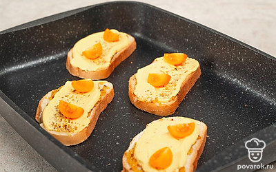 Приготовьте тосты. Смажьте ломтики хлеба зерновой горчицей, сырным соусом, украсьте дольками помидора черри, выложите их на противень и поставьте в духовку на 10 минут при температуре 200 градусов.