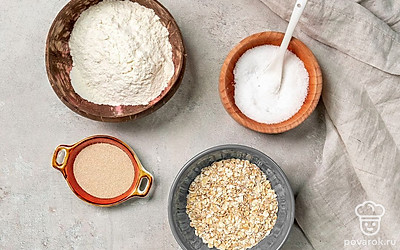 Овсяные хлопья измельчите в блендере или кофемолке и просейте. Отдельно просейте пшеничную муку, а затем соедините с овсяной. Воду прокипятите и остудите, чтобы она была теплой. Форму для выпечки застелите пергаментной бумагой.