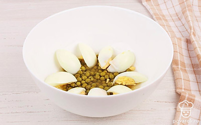 Возьмите глубокую тарелку или форму для выпечки. Выложите на ее дно небольшой слой консервированного горошка, а сверху положите немного нарезанных отварных яиц.