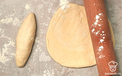 Приступите к формовке. По истечении указанного времени тесто выложите из миски на стол, немного обомните, разделите на две части. Каждую скатайте в шар, затем растяните руками в пласт и сверните рулетом.