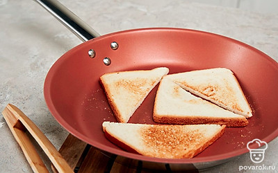 Обжарьте тосты. Ломтики хлеба разрежьте на два треугольника. Обжарьте заготовки на сковороде до золотистой корочки. Выложите на тарелку и оставьте слегка остыть.