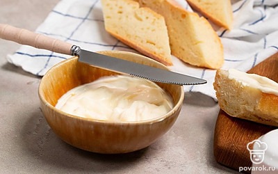 Подготовьте ингредиенты перед запеканием. На головке сыра сделайте надрезы в виде сетки до половины глубины. В миске смешайте майонез и сушеный чеснок. Противень застелите пергаментом. Кусочки багета смажьте майонезом с чесноком.