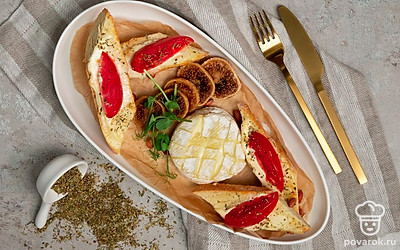 Пергамент обрежьте по диаметру сыра и с помощью лопатки переложите его в середину сервирочного блюда. Вокруг сыра выложите кусочки багета. Украсьте блюдо листьями базилика и петрушки.