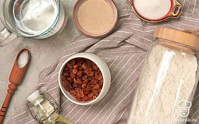 Отмерьте необходимое количество продуктов. Изюм замочите в теплой воде на 10-15 минут, затем промойте, обсушите на бумажных полотенцах. Воду подогрейте. Муку просейте через сито. Противень застелите пекарской бумагой, припылите мукой.