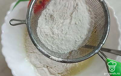 Добавьте ряженку. Просейте в тарелку муку через сито, перемешайте.